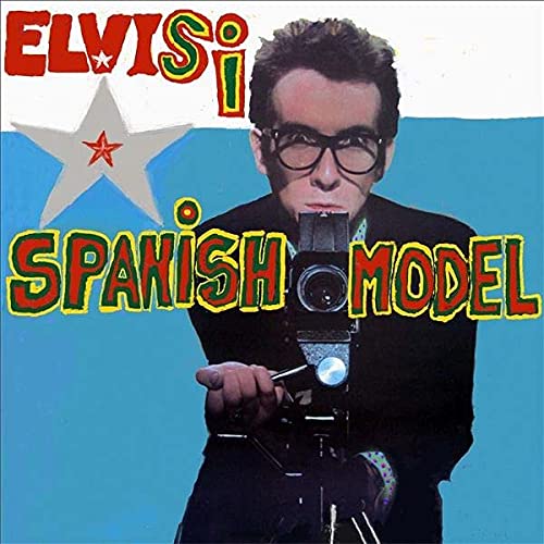 Album cover: man with glasses holding a camera, colorful text.