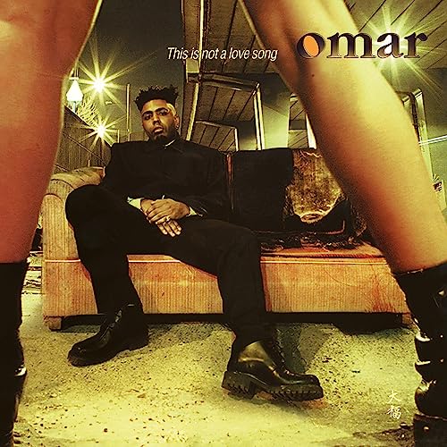 Omar sits on a couch framed by legs in boots, album cover.