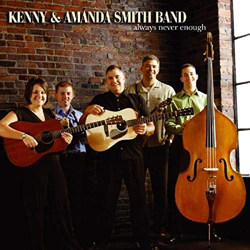 Five musicians with guitars and a bass stand against a brick wall.