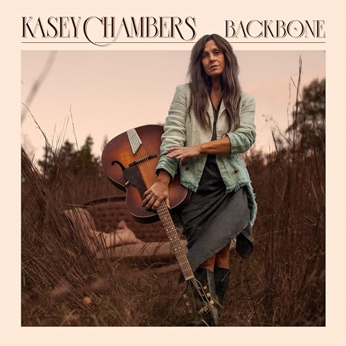 Kasey Chambers poses with an acoustic guitar in a field.