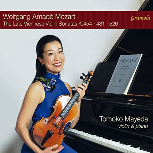 Violinist Tomoko Mayeda with violin, posing by a grand piano.