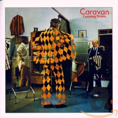 A person in a diamond-patterned suit stands in a dressing room with another man.