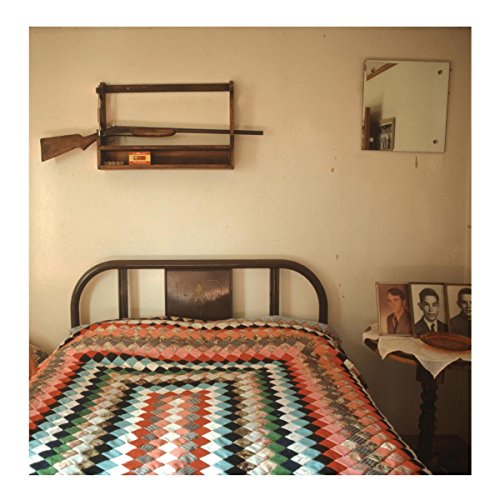 Bedroom scene with a record on the bed, gun rack, and photos.