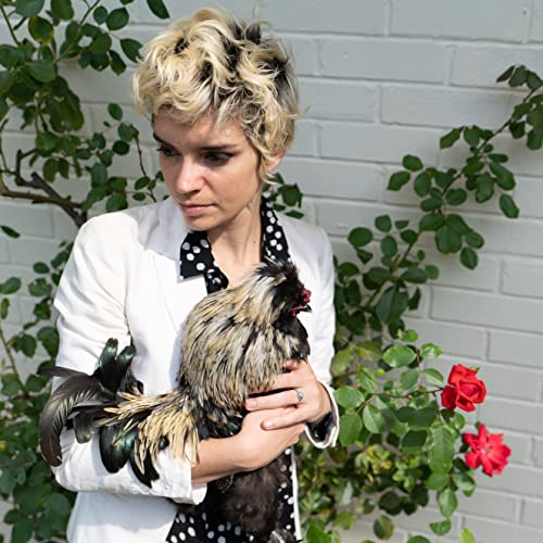Woman holding a black and gold rooster in front of greenery.