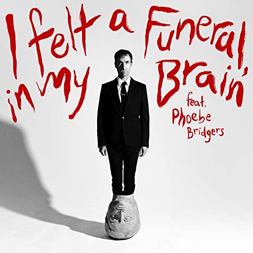 Andrew Bird in suit stands on a stone head, red text overlay.