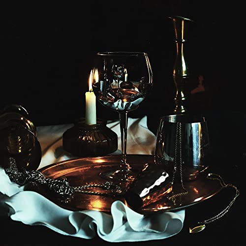Dark still life with glassware, candle, and metallic chain on fabric.