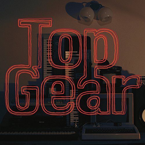 Red neon “Top Gear” sign over vintage electronics and a keyboard.