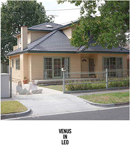 Cream-colored house with two people sitting on the driveway.