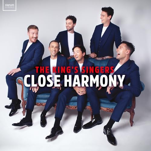 Six men, The King’s Singers, in dark suits on a blue sofa.