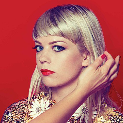 Blonde woman with red lips and floral patterned clothing, against red.