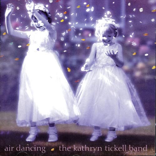 Two young girls in white dresses dance amidst falling confetti.