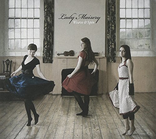 Three women in dresses pose in a room with windows and a violin.