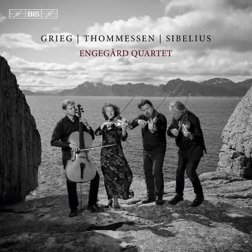 Black and white photo of a string quartet playing outdoors by water.