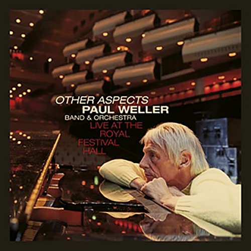 Paul Weller at a piano on stage, concert hall lighting above.