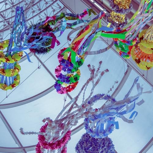 Colorful, hanging sculptures made of paper and streamers fill the space.