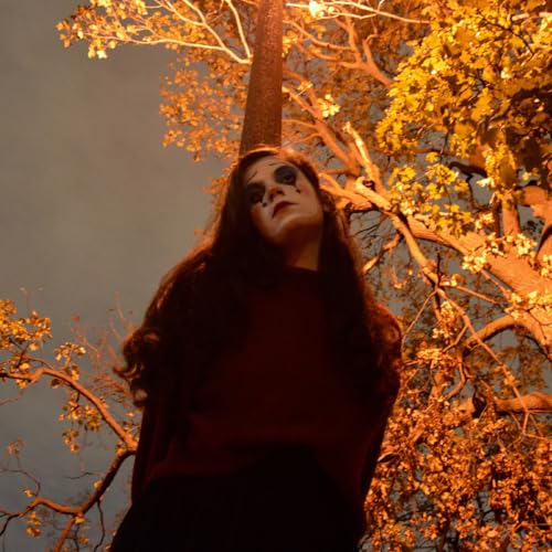 Woman with dark makeup looks up toward illuminated tree branches.