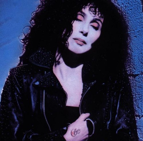 Cher with dark, curly hair wearing a black leather jacket.