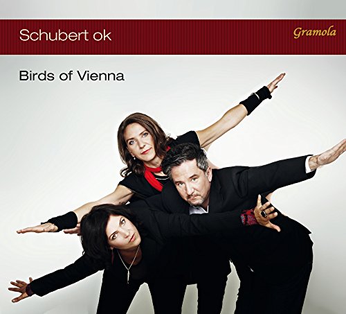 Three people in suits pose with arms outstretched, mimicking bird wings.