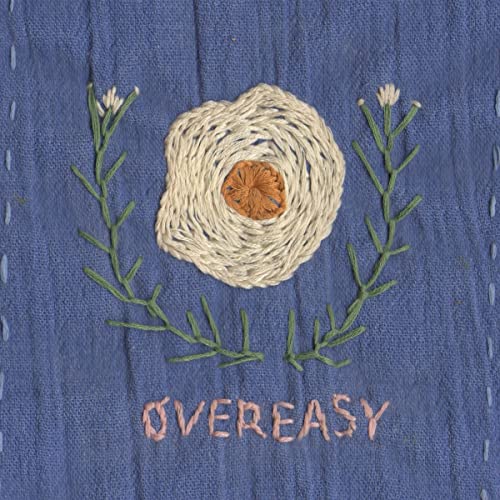 Embroidered fried egg with flowers and the text “Overeasy” on blue fabric.