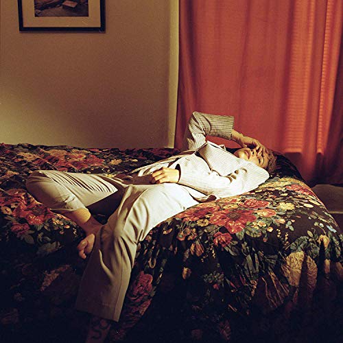 Person lying on floral bed, head covered with hand, indoors.