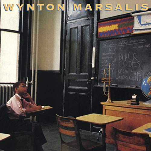 A young boy sits at a school desk in a classroom with a chalkboard.