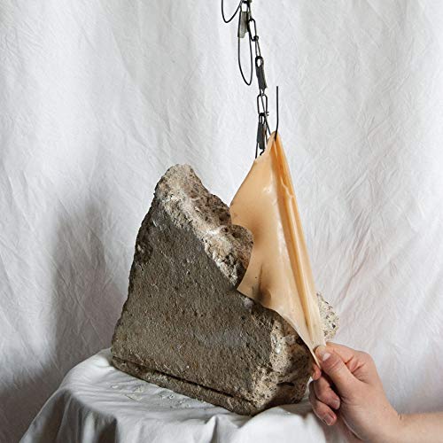 Hand peeling back peach-colored material from a grey rock formation.
