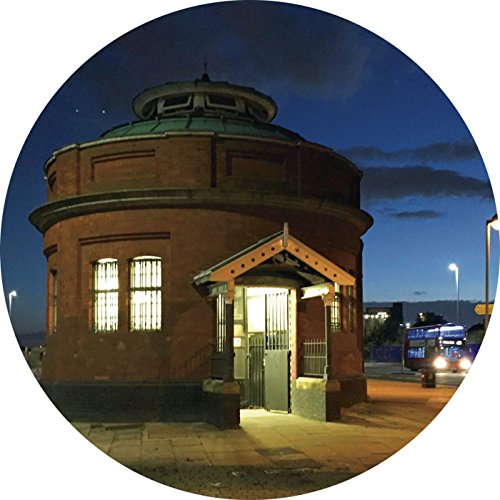 Round image of a brick building with a green roof at dusk.