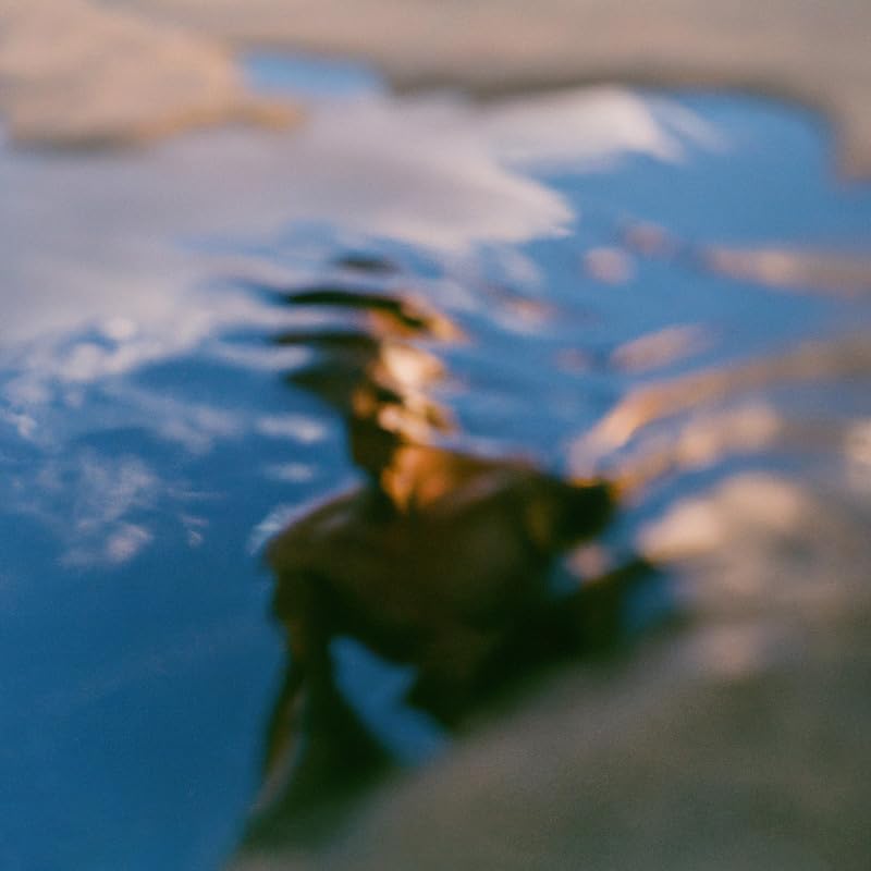 Blurred image of a person’s face reflected in rippling blue water.