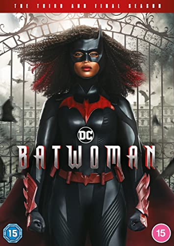 Batwoman in superhero costume stands before ornate iron gates.