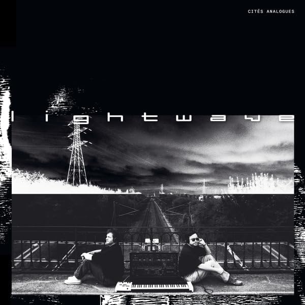 Vinyl record cover: two figures with synthesizers, cityscape backdrop.