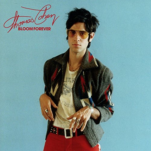 AlbumCandid portrait of Thomas Cohen wearing sunglasses and a patterned jacket against blue background.