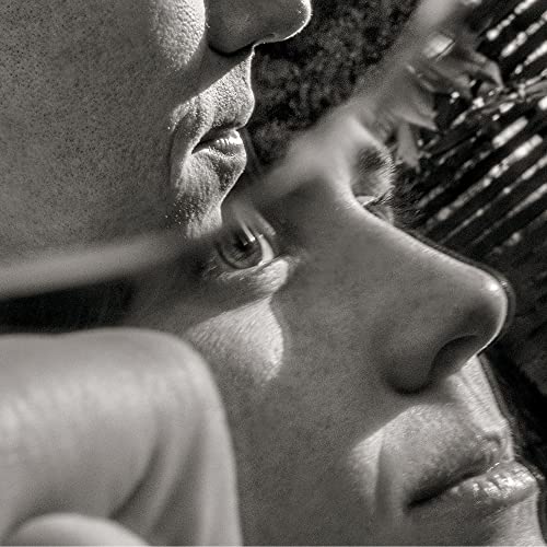 Black and white close-up of two faces, partially obscured by foliage.