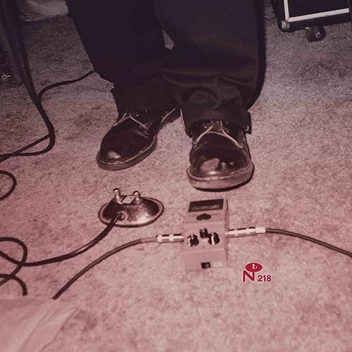 Feet with shoes standing on carpet near guitar effect pedals.