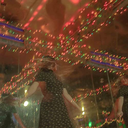 Woman with flowing hair dances beneath colorful string lights.