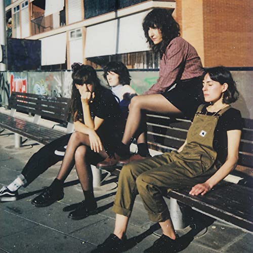 Four people sit on a bench in front of graffiti-covered walls.