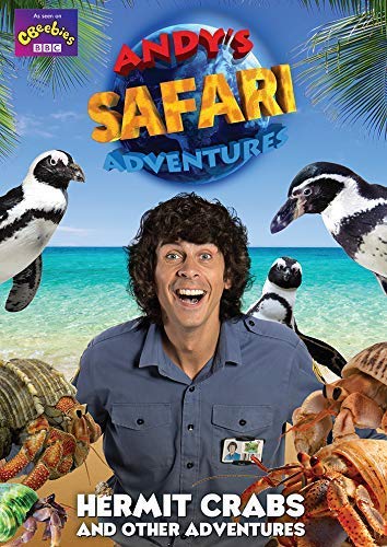 Andy Day smiling in a safari shirt with penguins and hermit crabs on beach.
