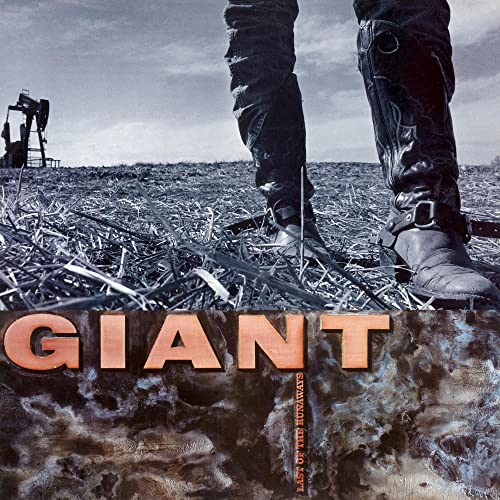 Cowboy boots standing in a field with an oil pump in the distance.