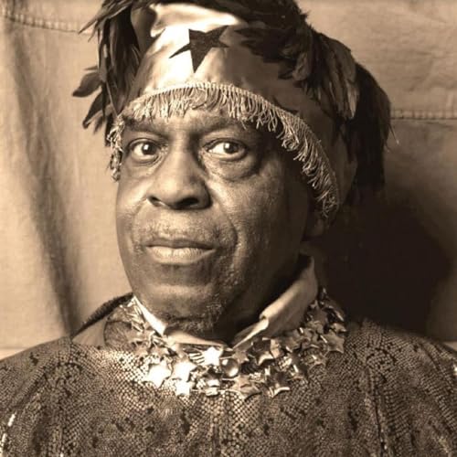 Close-up portrait of Sun Ra wearing a feathered headdress and ornate collar.
