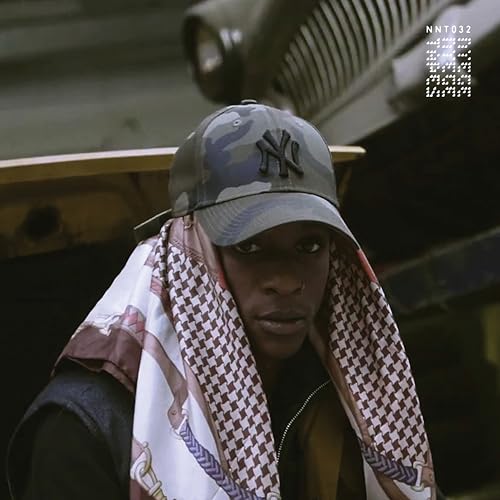 Man wearing a cap and patterned scarf, with a tank in background.