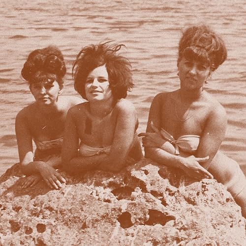 Three women with curly hair pose on rocks by the water.