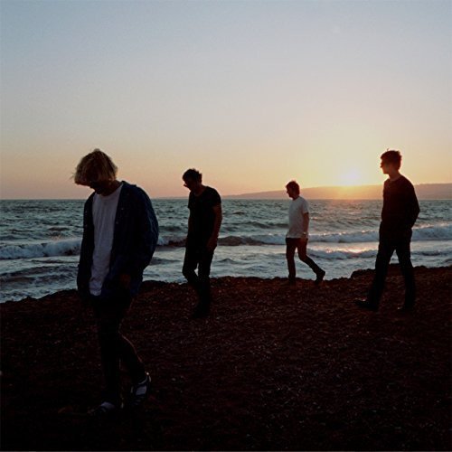 Four figures walking on a beach at sunset, silhouetted.