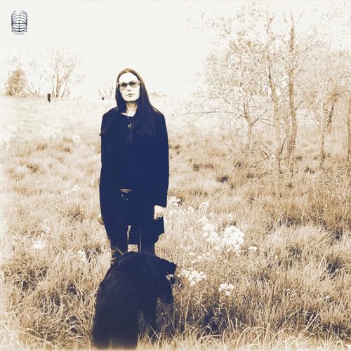 Woman with a black dog standing in a field of dry grass.