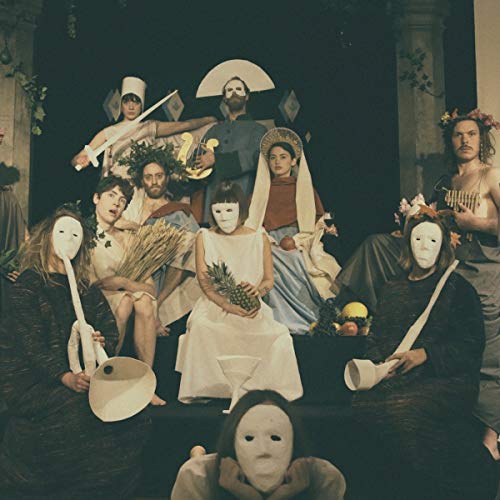 Group portrait of people wearing masks, holding objects, in a dimly lit room.