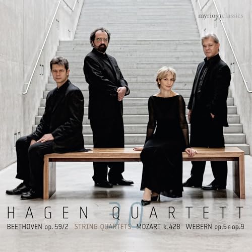 The Hagen Quartett members in black attire sit and stand on a wooden bench.