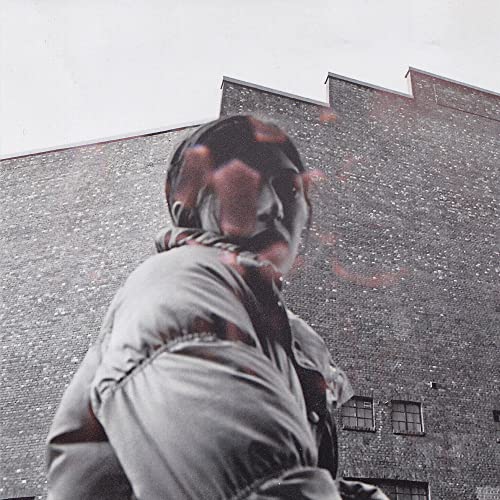 A person in a puffer jacket stands before a large, textured brick building.