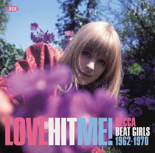 Album cover featuring a young woman among purple flowers, text “Love Hit Me!”.