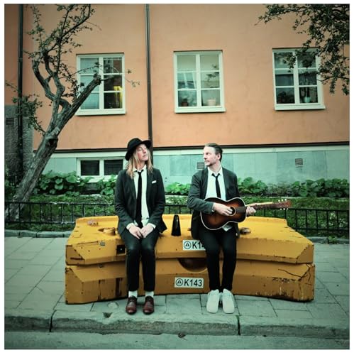 Two musicians with a guitar sit on a yellow concrete barrier.