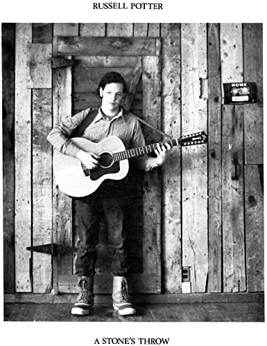 Black and white photo of a man with a guitar, standing by a door.
