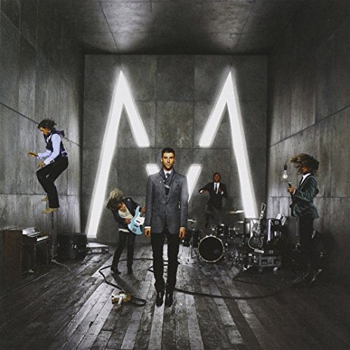 Maroon 5 band members in a concrete room with a large illuminated "M".