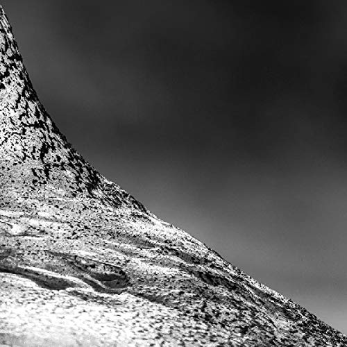 Black and white close-up of a textured, rocky hillside under a cloudy sky.